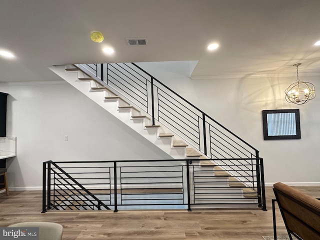 staircase featuring an inviting chandelier, ornamental molding, and wood-type flooring