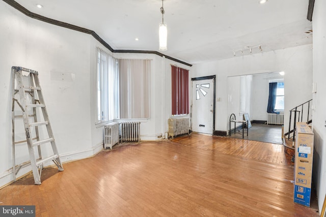 unfurnished living room with wood-type flooring, radiator heating unit, and crown molding