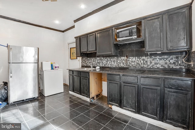 kitchen featuring appliances with stainless steel finishes, washer / dryer, sink, decorative backsplash, and dark tile patterned floors