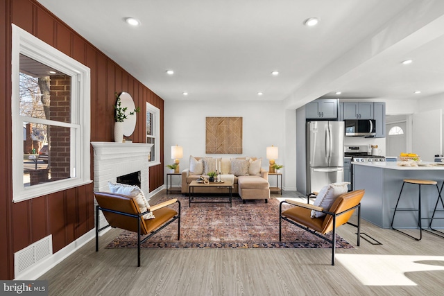 living area featuring light wood finished floors, plenty of natural light, a fireplace, and visible vents