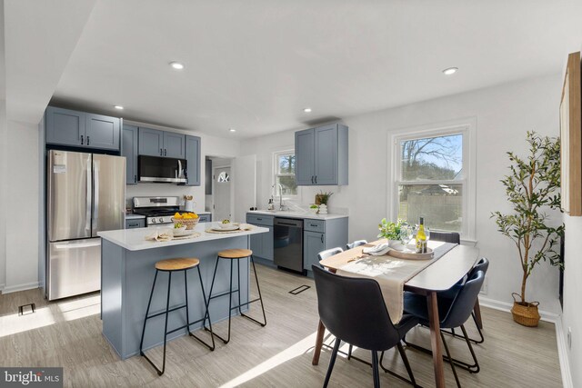 kitchen with light wood finished floors, a breakfast bar area, stainless steel appliances, light countertops, and a sink