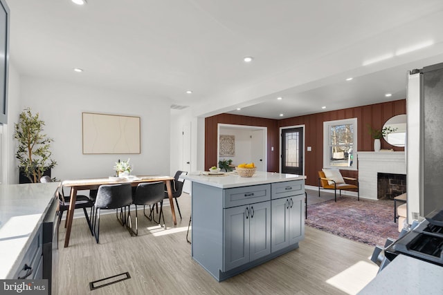 kitchen with light wood-style flooring, a kitchen island, gray cabinets, light countertops, and a brick fireplace