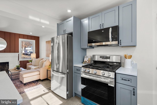 kitchen featuring a fireplace, light wood finished floors, stainless steel appliances, light countertops, and open floor plan