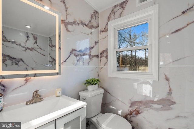 bathroom with visible vents, stone wall, toilet, and vanity