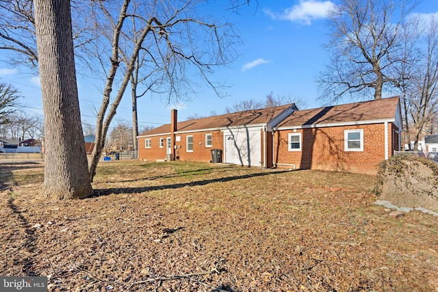 rear view of house with an attached garage, a yard, a chimney, and brick siding