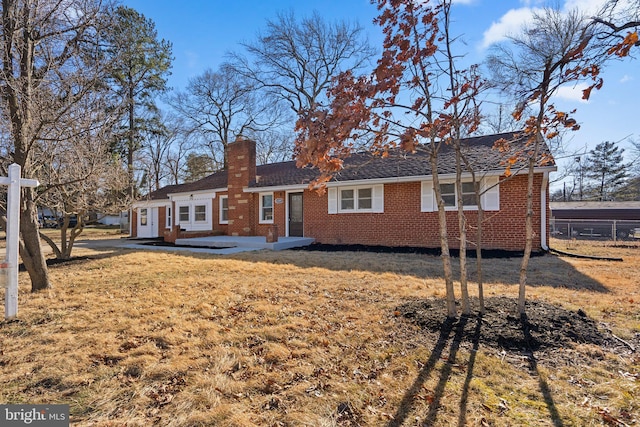 rear view of house featuring brick siding, a lawn, and a chimney