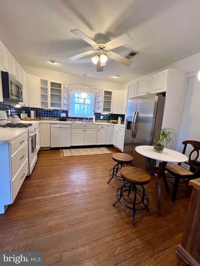 kitchen with pendant lighting, appliances with stainless steel finishes, white cabinetry, dark hardwood / wood-style floors, and decorative backsplash