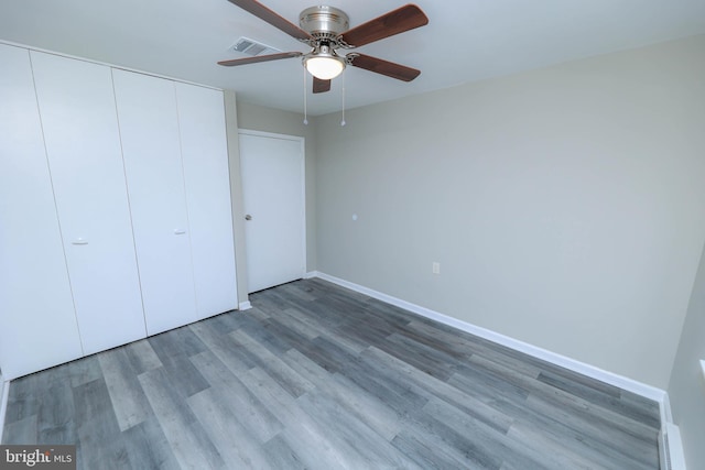 unfurnished bedroom with ceiling fan, wood finished floors, visible vents, baseboards, and a closet