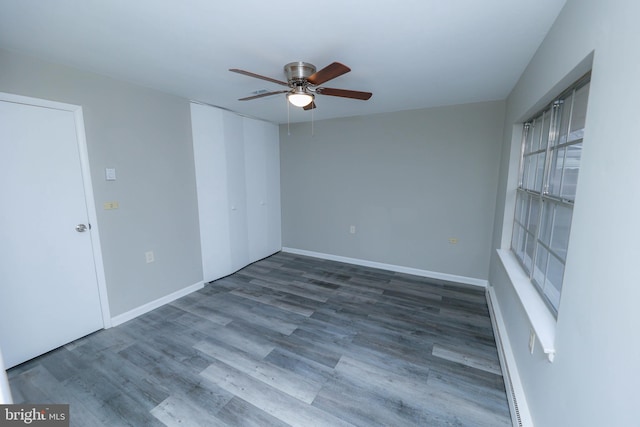 spare room with a baseboard heating unit, ceiling fan, baseboards, and wood finished floors