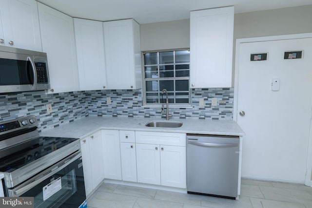 kitchen with appliances with stainless steel finishes, white cabinetry, sink, backsplash, and light stone countertops