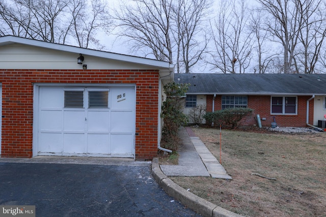 ranch-style home with a garage, central AC unit, aphalt driveway, and brick siding