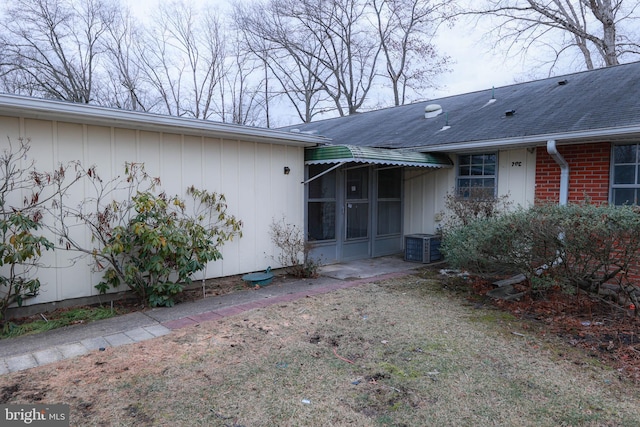 doorway to property featuring a shingled roof and brick siding