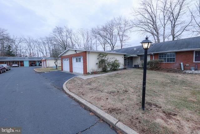 single story home with driveway, an attached garage, a front lawn, and brick siding