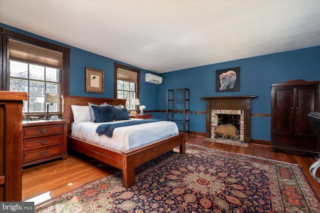 bedroom featuring wood finished floors, a fireplace, and a wall mounted AC