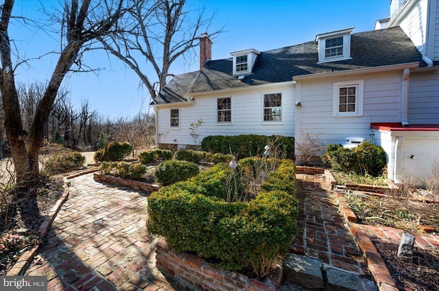 back of house with a patio area, a shingled roof, a chimney, and a vegetable garden