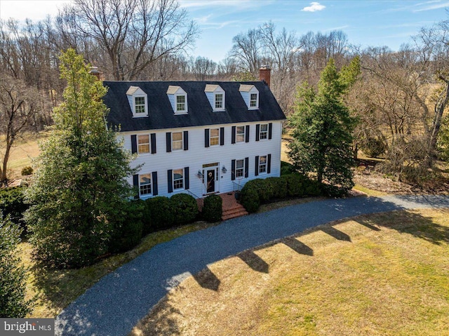 view of front facade with driveway, a chimney, and a front lawn