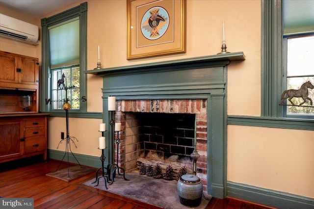 interior details with a brick fireplace, an AC wall unit, baseboards, and wood finished floors