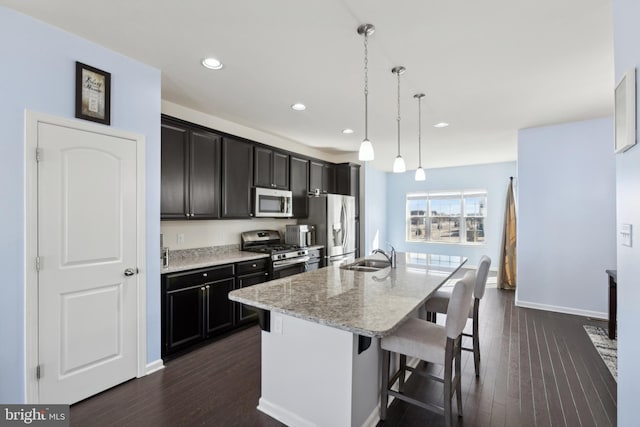 kitchen with a center island with sink, decorative light fixtures, light stone countertops, appliances with stainless steel finishes, and a kitchen bar