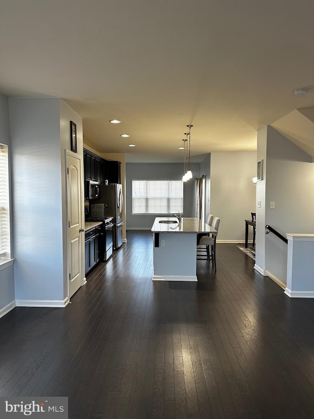 kitchen featuring an island with sink, stainless steel appliances, dark hardwood / wood-style flooring, decorative light fixtures, and sink