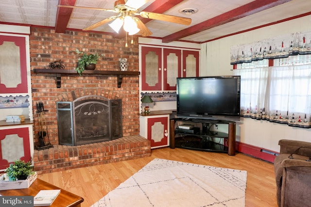 living room featuring a brick fireplace, a ceiling fan, beam ceiling, and wood finished floors