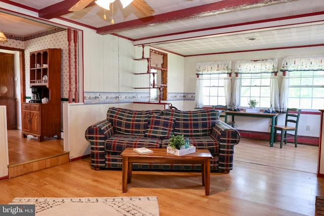 living area featuring light wood finished floors, wallpapered walls, a ceiling fan, and beamed ceiling