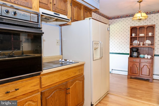 kitchen with pendant lighting, under cabinet range hood, a baseboard heating unit, black appliances, and wallpapered walls