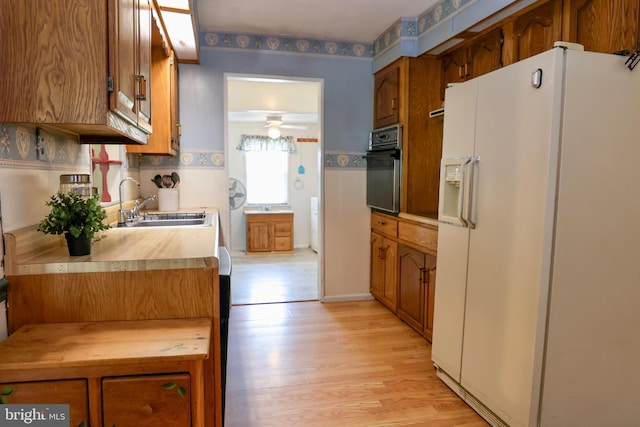 kitchen featuring white fridge with ice dispenser, brown cabinetry, light countertops, and black oven