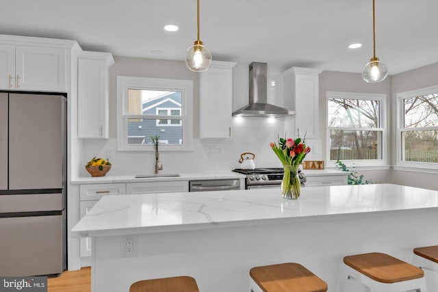 kitchen featuring pendant lighting, wall chimney range hood, stainless steel appliances, and sink