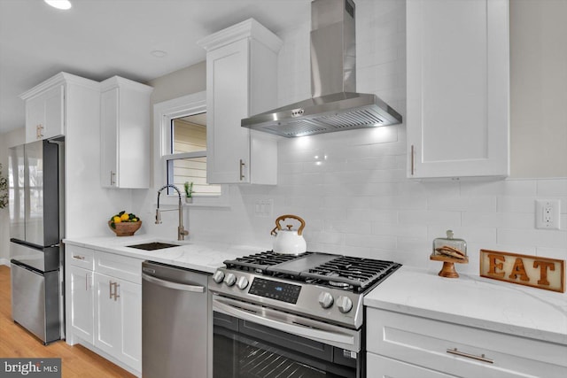 kitchen with wall chimney range hood, sink, appliances with stainless steel finishes, white cabinetry, and light stone counters