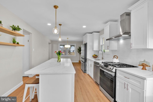 kitchen featuring wall chimney exhaust hood, white cabinetry, light stone counters, pendant lighting, and stainless steel appliances