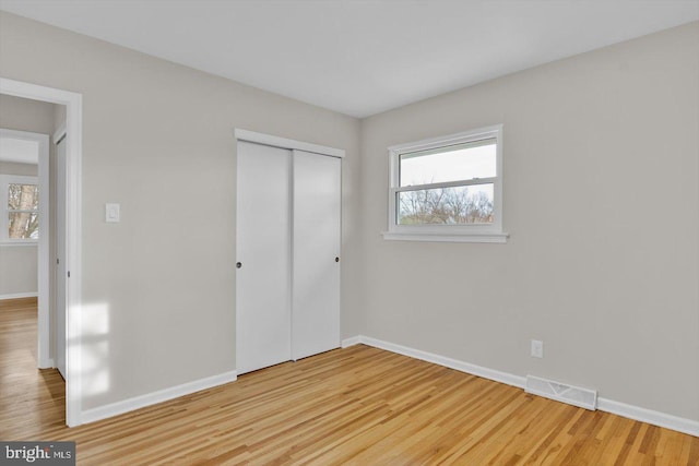 unfurnished bedroom with multiple windows, light wood-type flooring, and a closet