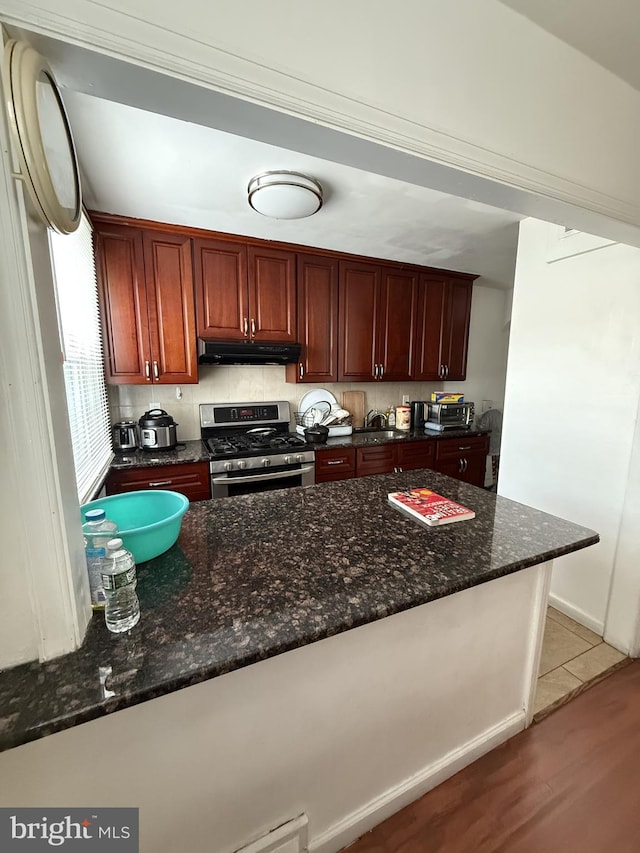 kitchen featuring decorative backsplash, dark stone counters, kitchen peninsula, gas stove, and light wood-type flooring