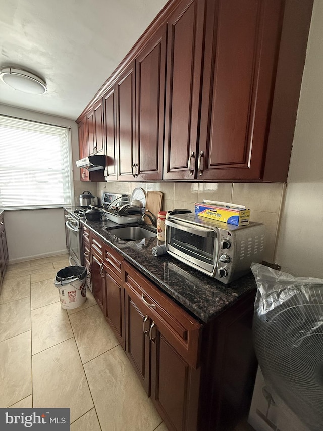 kitchen featuring sink, dark stone countertops, tasteful backsplash, stainless steel gas range oven, and light tile patterned flooring