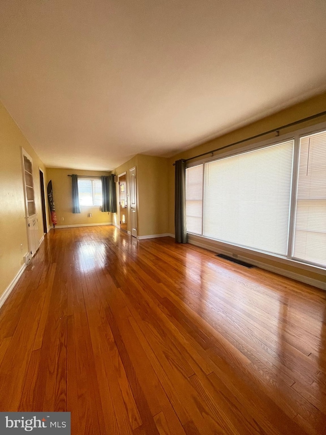 unfurnished living room featuring baseboards, wood-type flooring, and built in shelves