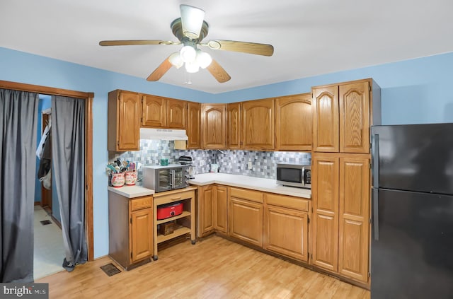 kitchen featuring ceiling fan, black fridge, light hardwood / wood-style floors, and decorative backsplash