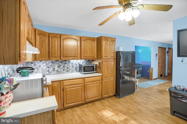 kitchen featuring ceiling fan, black refrigerator, light wood-type flooring, and decorative backsplash