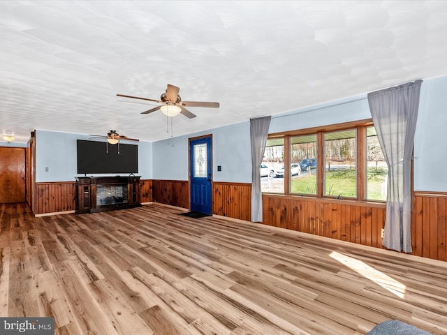 unfurnished living room with ceiling fan, wooden walls, and hardwood / wood-style floors