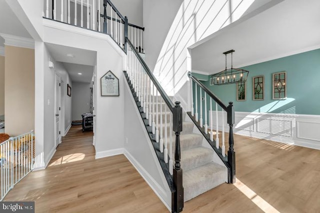 stairs with an inviting chandelier, hardwood / wood-style floors, crown molding, and a high ceiling