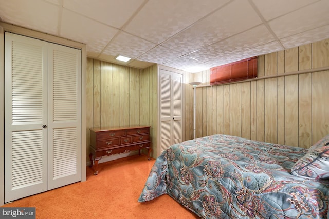 carpeted bedroom featuring two closets, a paneled ceiling, and wood walls