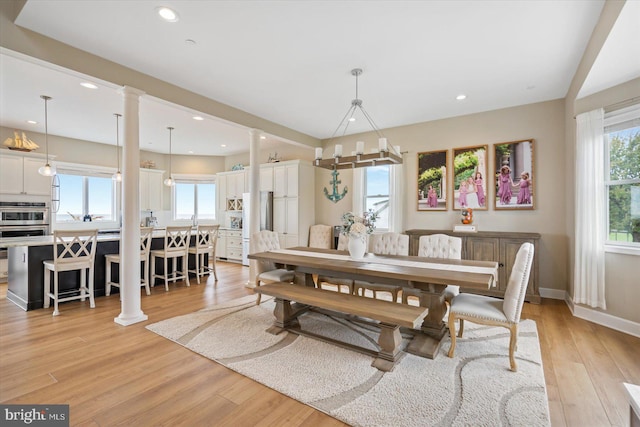 dining space featuring plenty of natural light, light wood-style flooring, and decorative columns