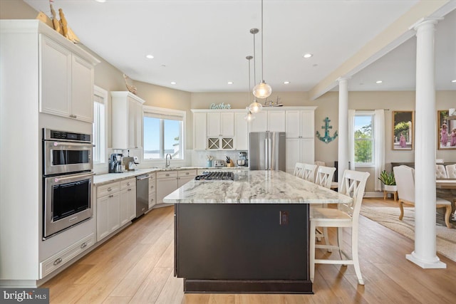 kitchen with a breakfast bar, a kitchen island, appliances with stainless steel finishes, light wood finished floors, and decorative columns