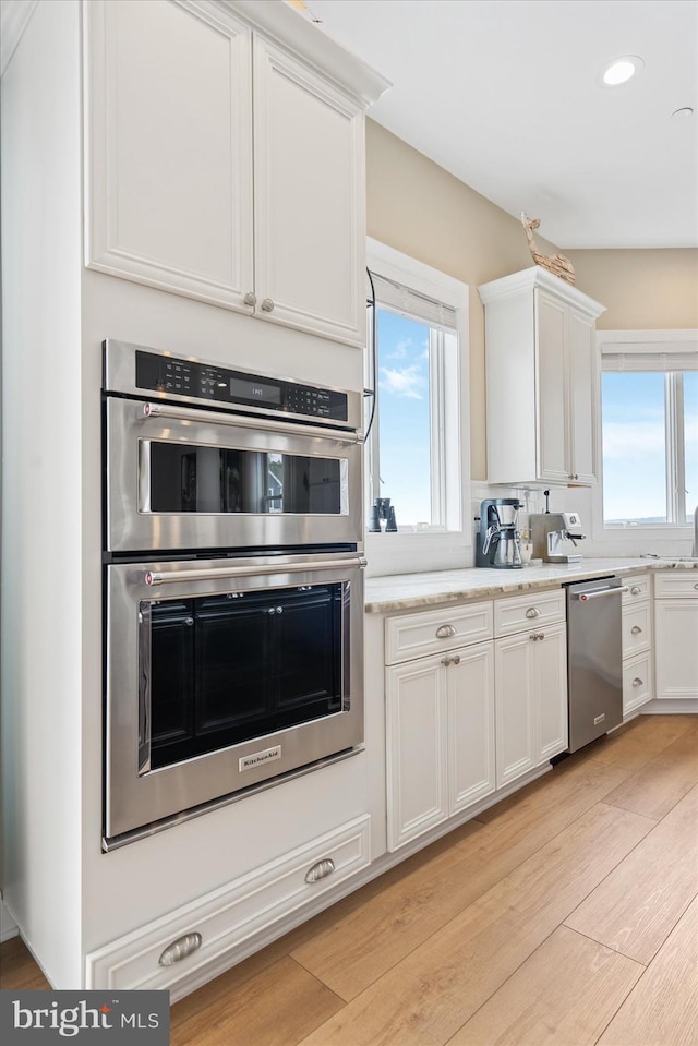 kitchen with stainless steel appliances, a healthy amount of sunlight, white cabinets, and light wood-type flooring