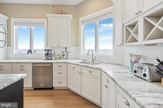 kitchen featuring sink, white cabinets, light hardwood / wood-style floors, a water view, and light stone countertops