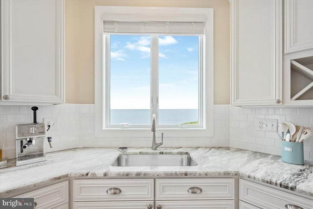 kitchen featuring light stone counters, sink, white cabinets, and a water view