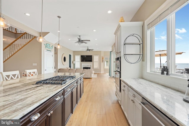 kitchen featuring recessed lighting, appliances with stainless steel finishes, a fireplace, light wood finished floors, and light stone countertops