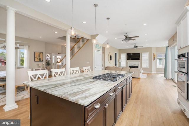 kitchen with open floor plan, a breakfast bar, light wood-type flooring, decorative columns, and stainless steel appliances