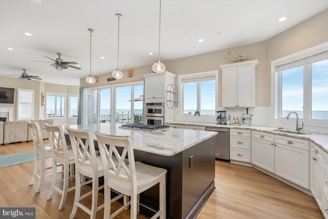 kitchen featuring light stone countertops, a kitchen island, a sink, stainless steel appliances, and open floor plan