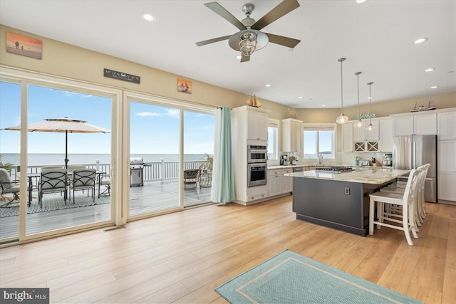 kitchen with appliances with stainless steel finishes, white cabinets, hanging light fixtures, a center island, and a water view