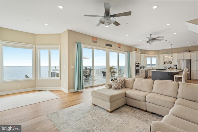 living room featuring ceiling fan, a water view, and light hardwood / wood-style floors