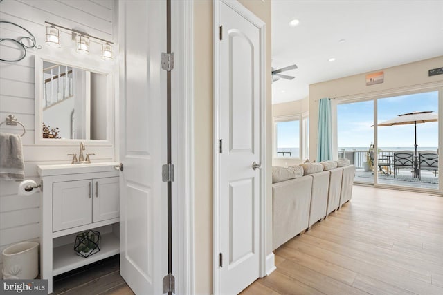 hall featuring light wood finished floors, recessed lighting, and a sink